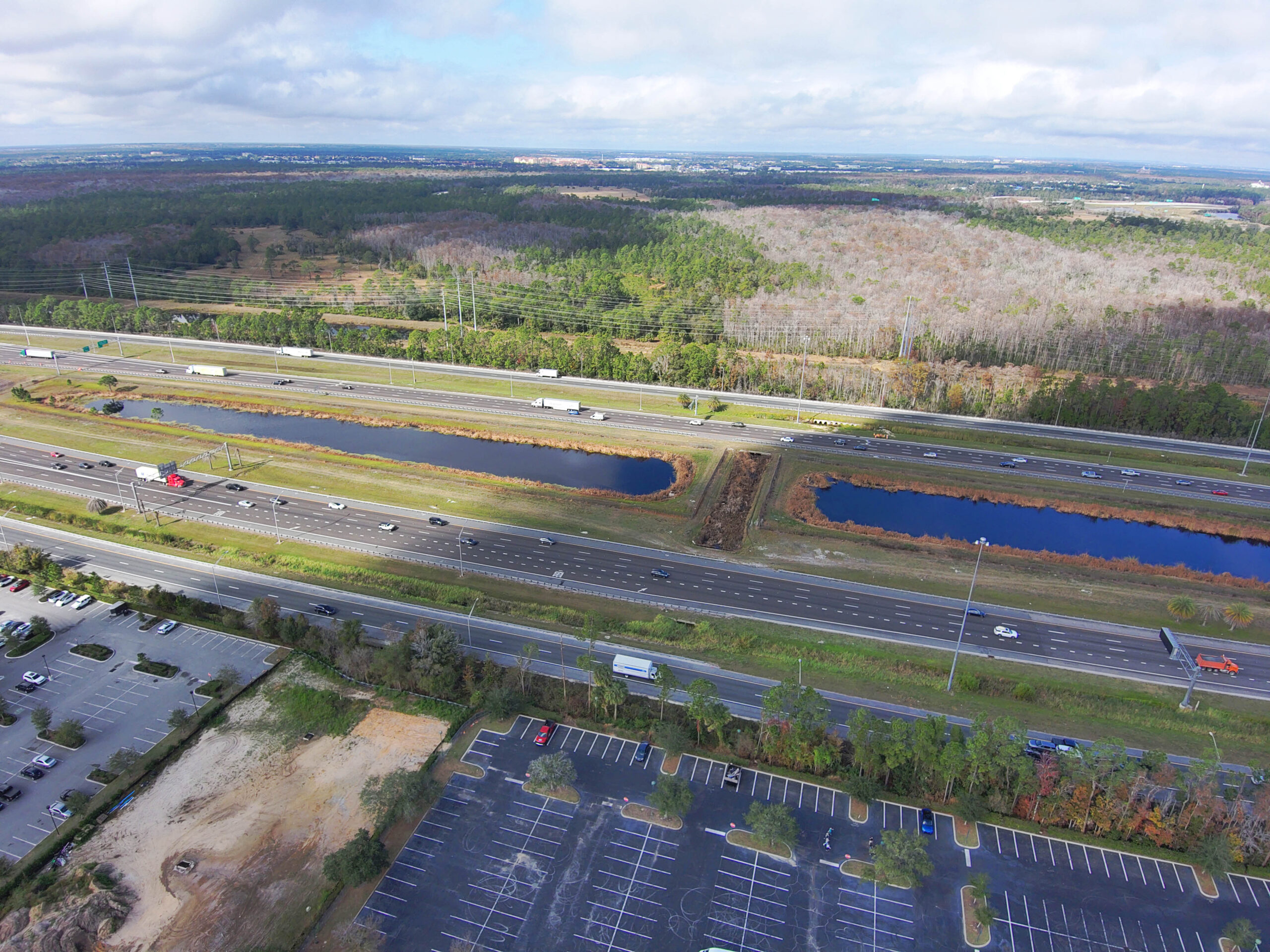 Aerial view of a highway with sparse traffic, flanked by green fields and trees