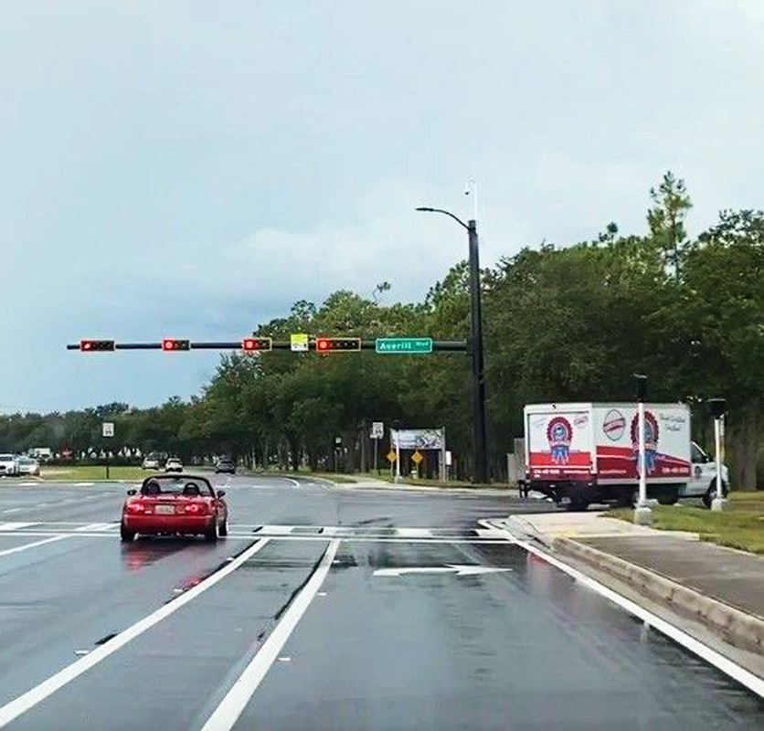 Red convertible turning at a wet intersection under a red traffic light, Averitt Road sign visible
