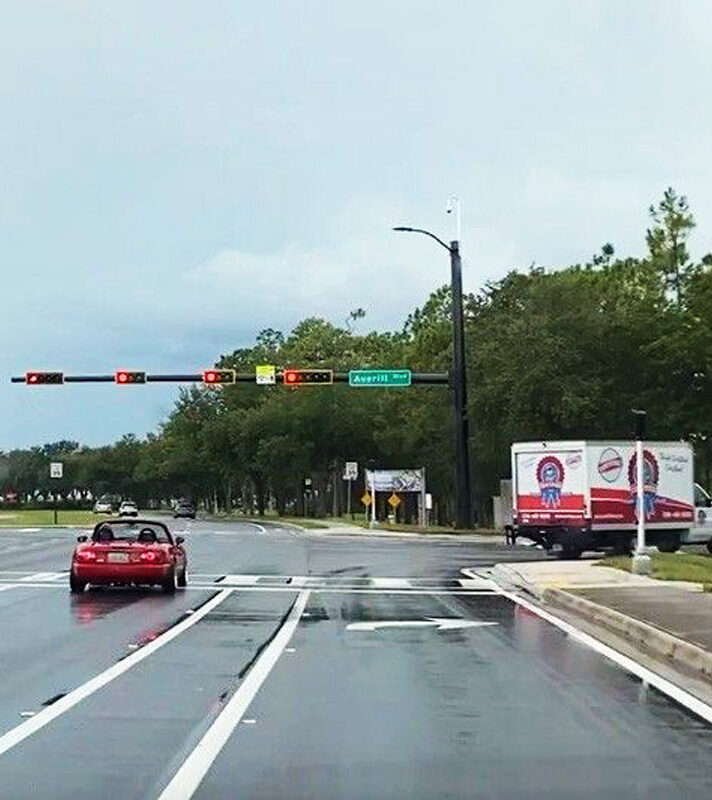 Red car approaches traffic lights on wet road, truck parked right