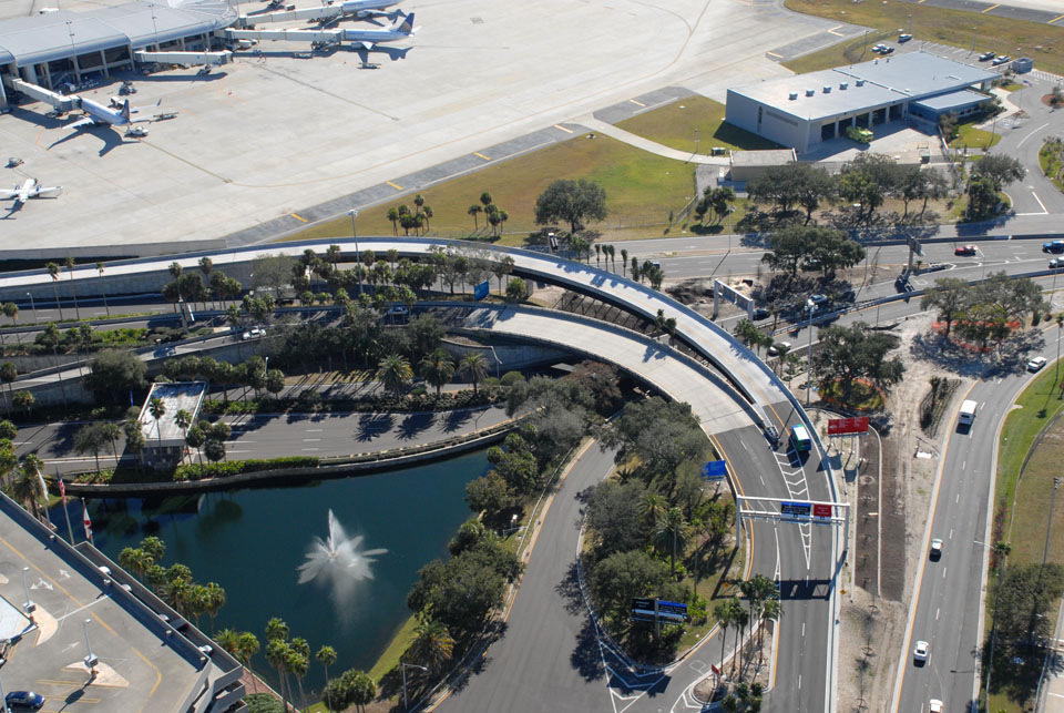 Aerial view of a recirculation bridge near an airport terminal, surrounded by roads and a water fountain below