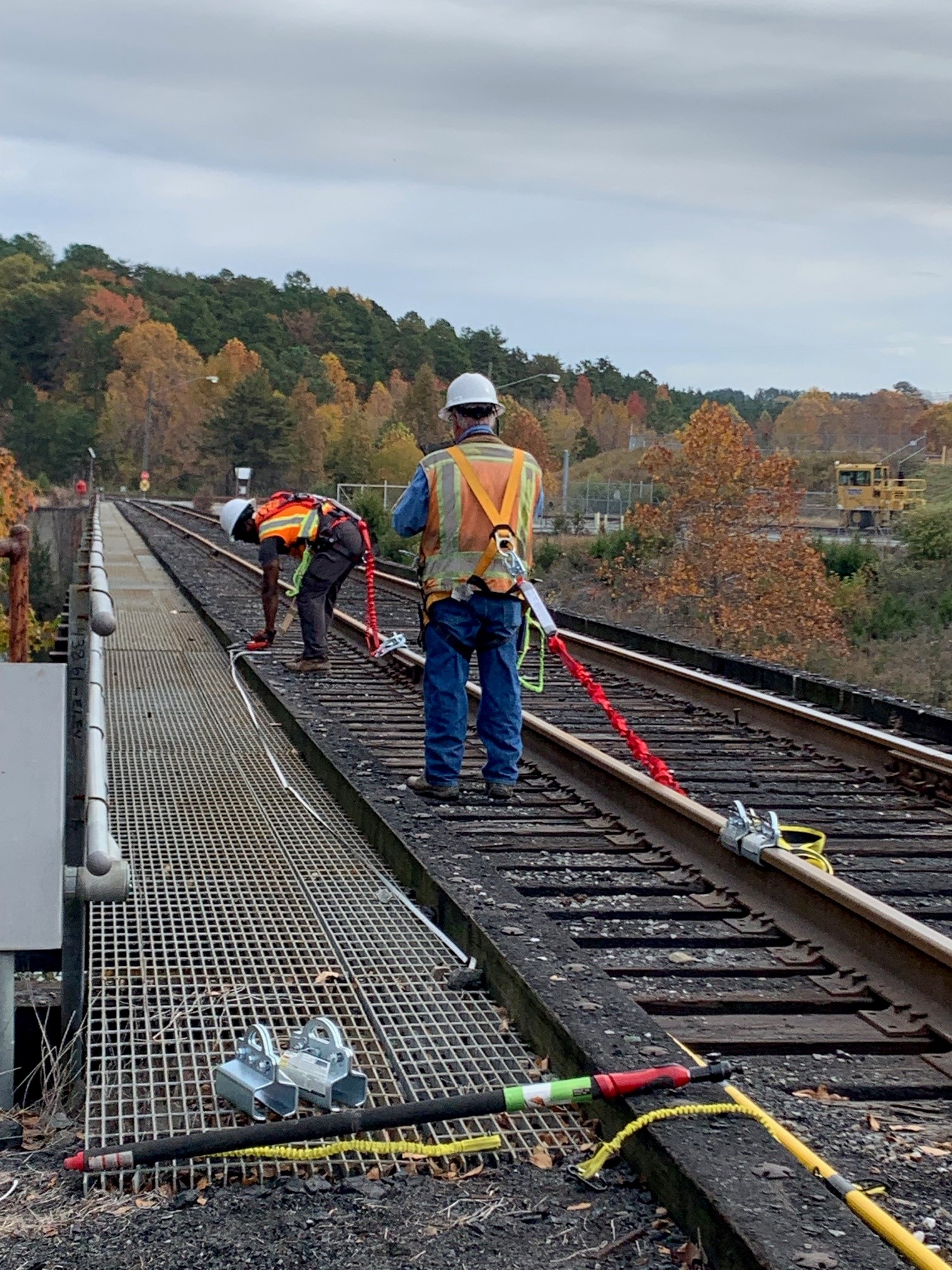 Two workers with safety gear inspect railway tracks on a bridge