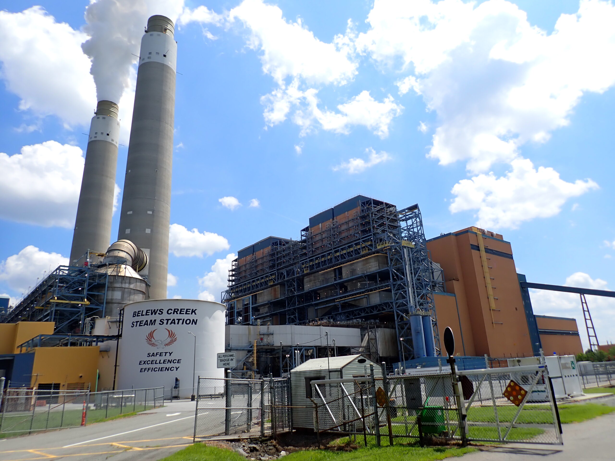 Belews Creek Steam Station with large smokestacks, clear sky, signage emphasizes safety, excellence, efficiency