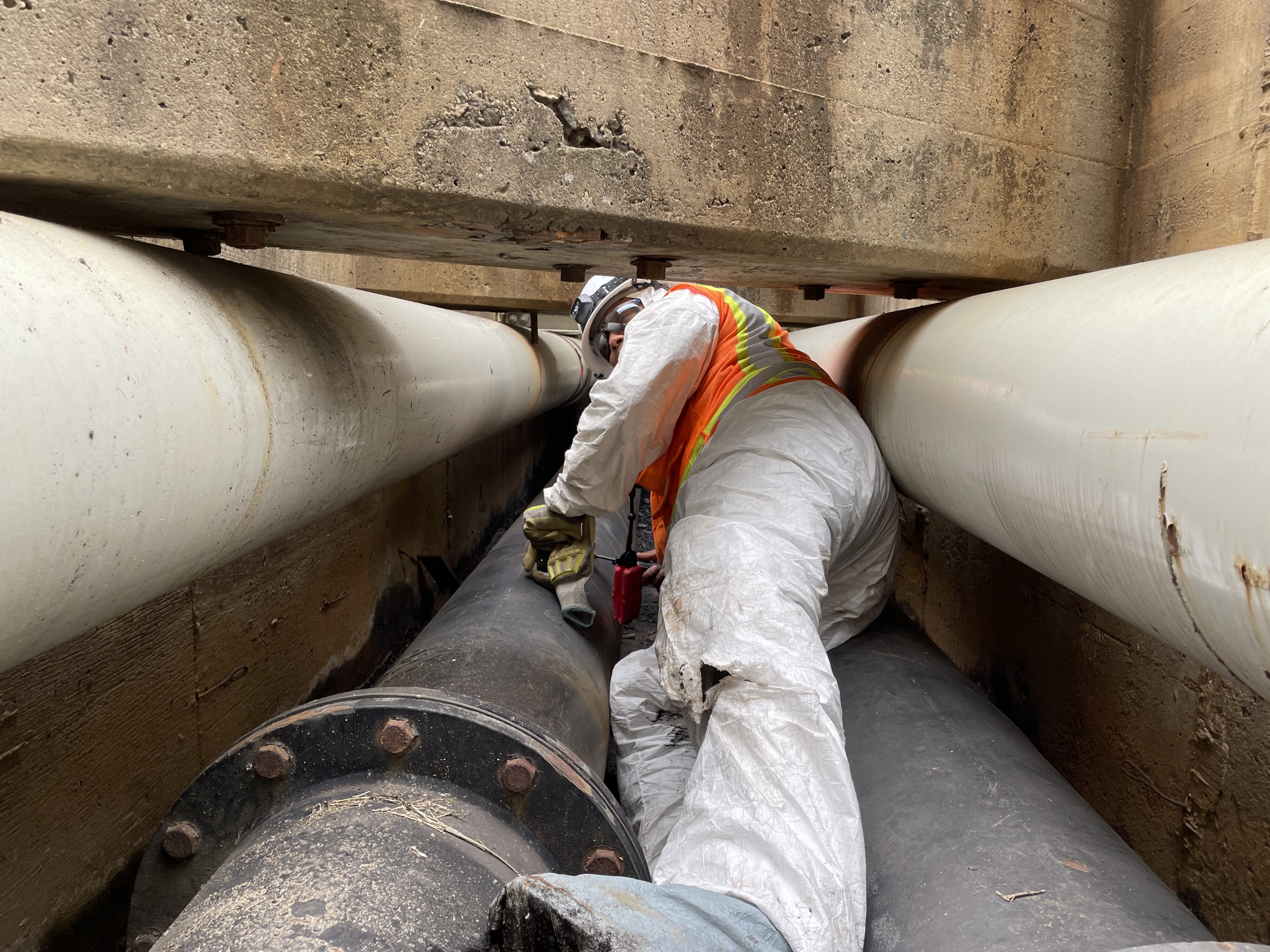 Worker in safety gear navigating between concrete walls and large pipes