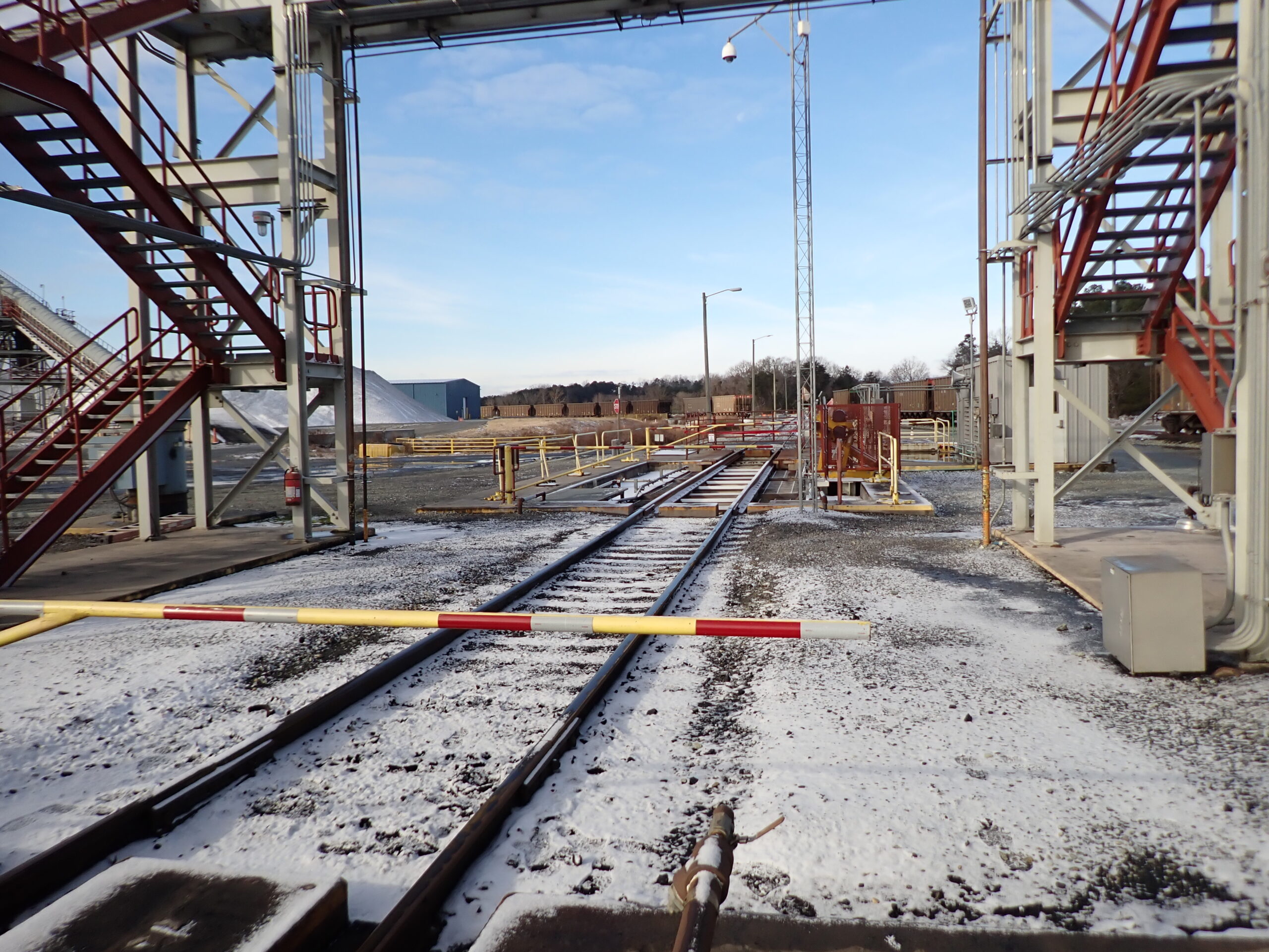 Railroad track with snow, flanked by metal structures and red staircases, under a clear sky