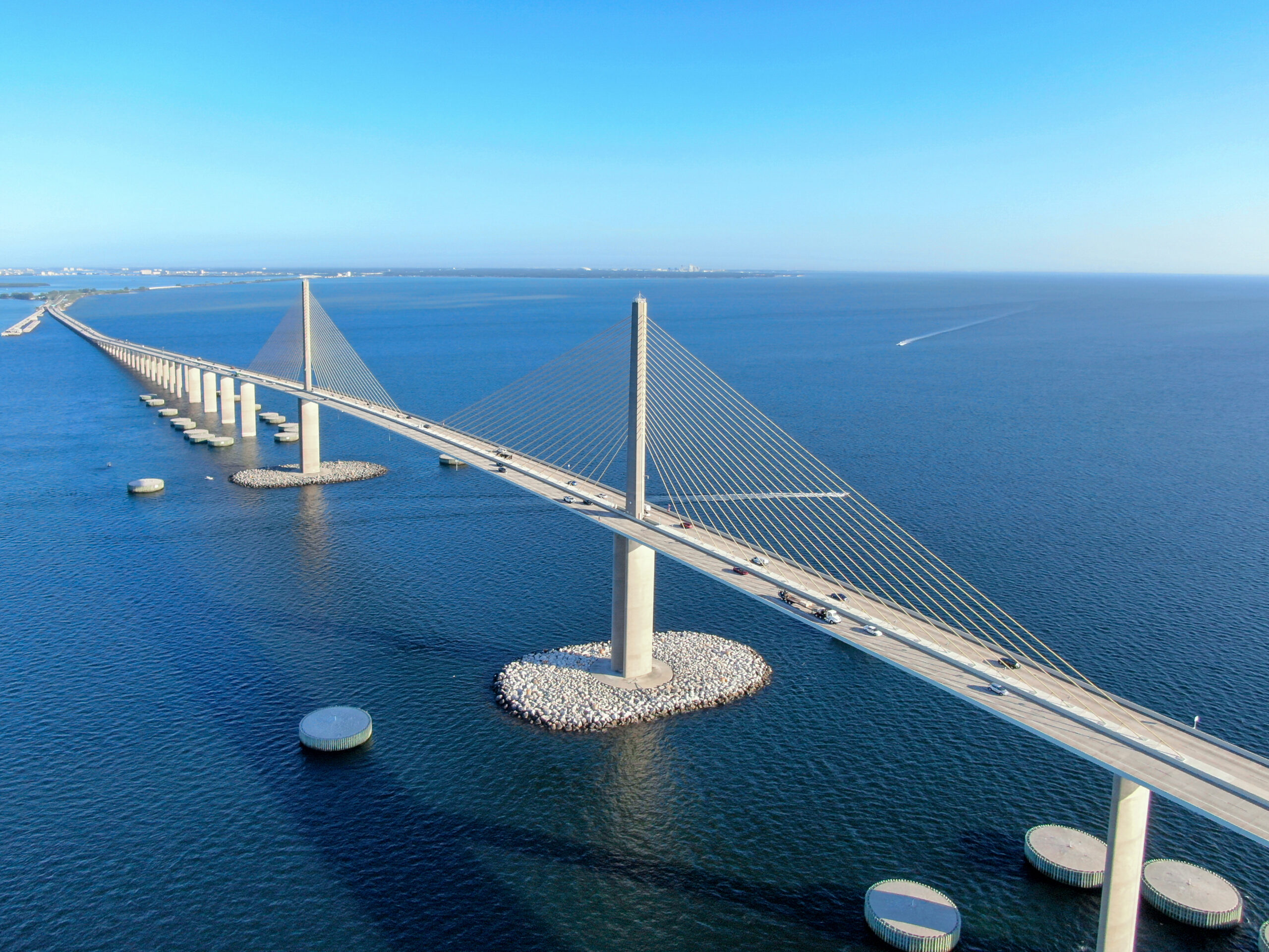 Suspension bridge over vast blue water, vehicles crossing, clear sky