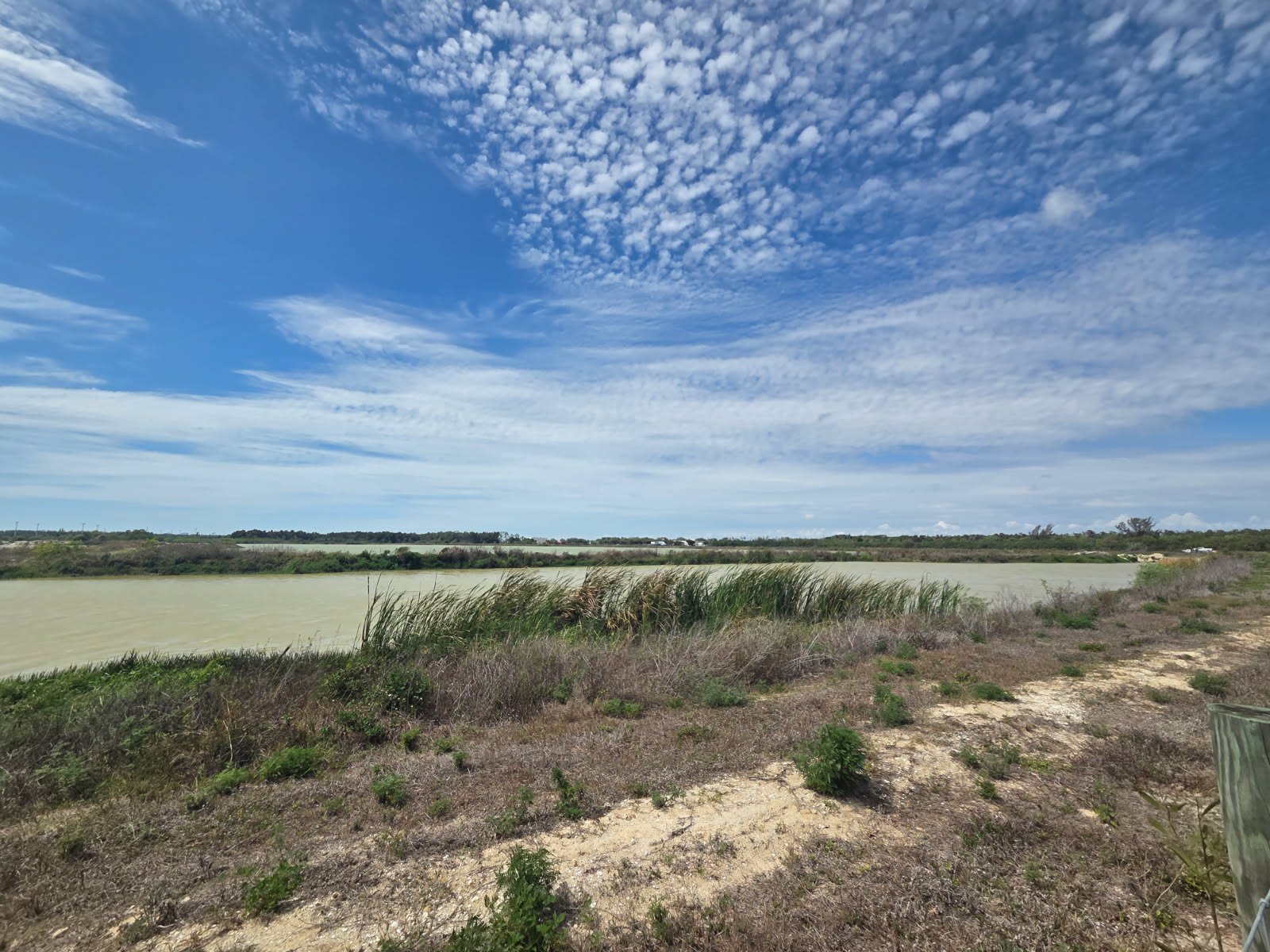Calm river with grassy banks and a wide, blue sky overhead