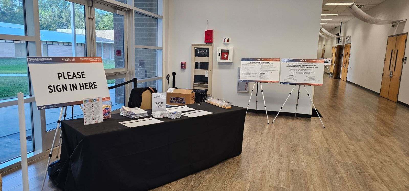 Sign-in table with papers in a hallway; sign reads "Please sign in here"