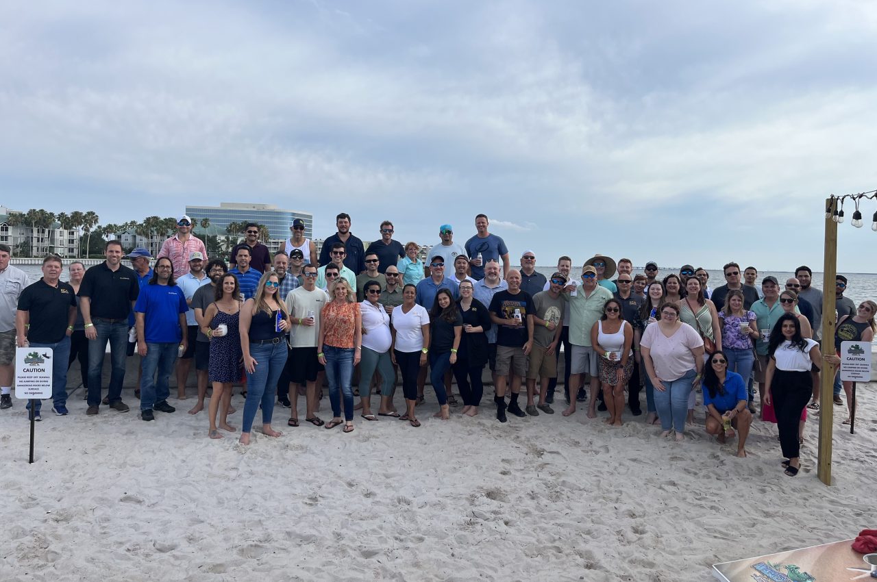 Group of people smiling on a sandy beach with a cloudy sky