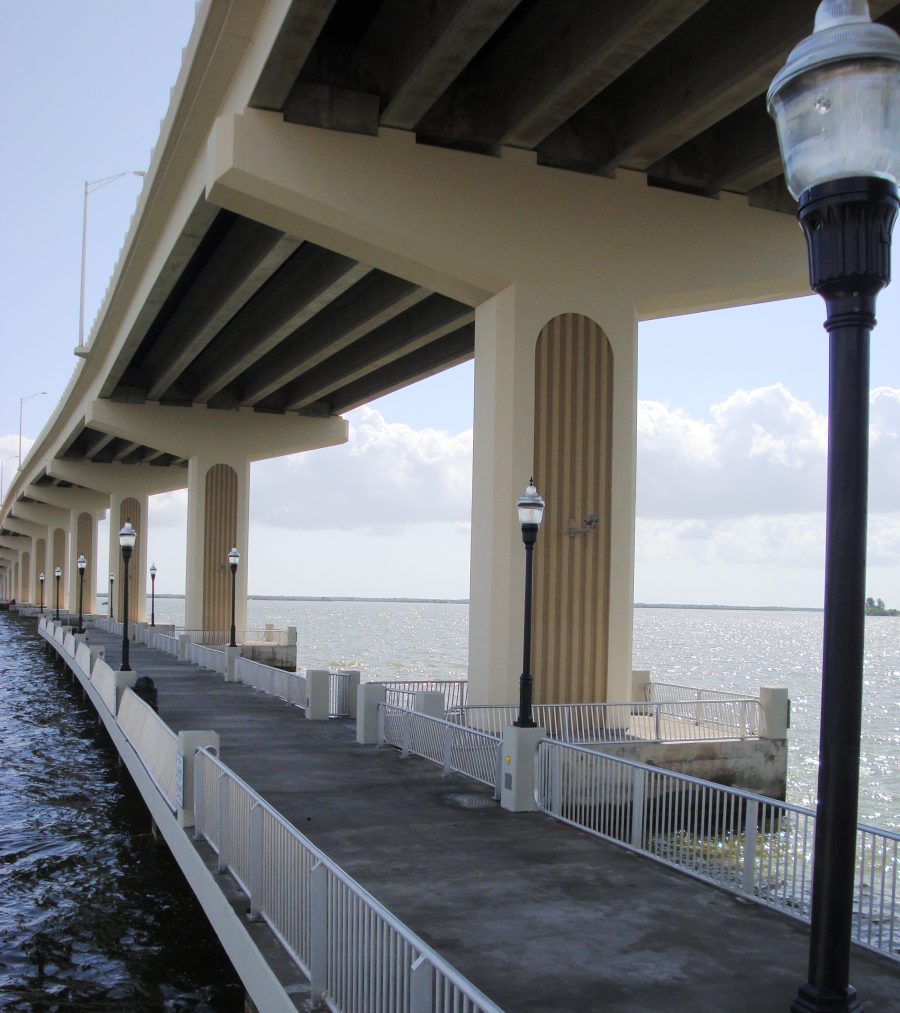 Fishing pier under a long bridge with metal railings and lampposts