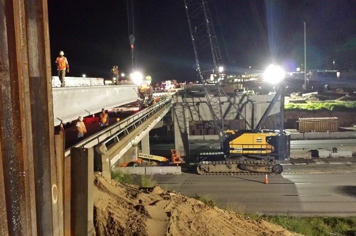 Construction crew working on a bridge at night under bright floodlights