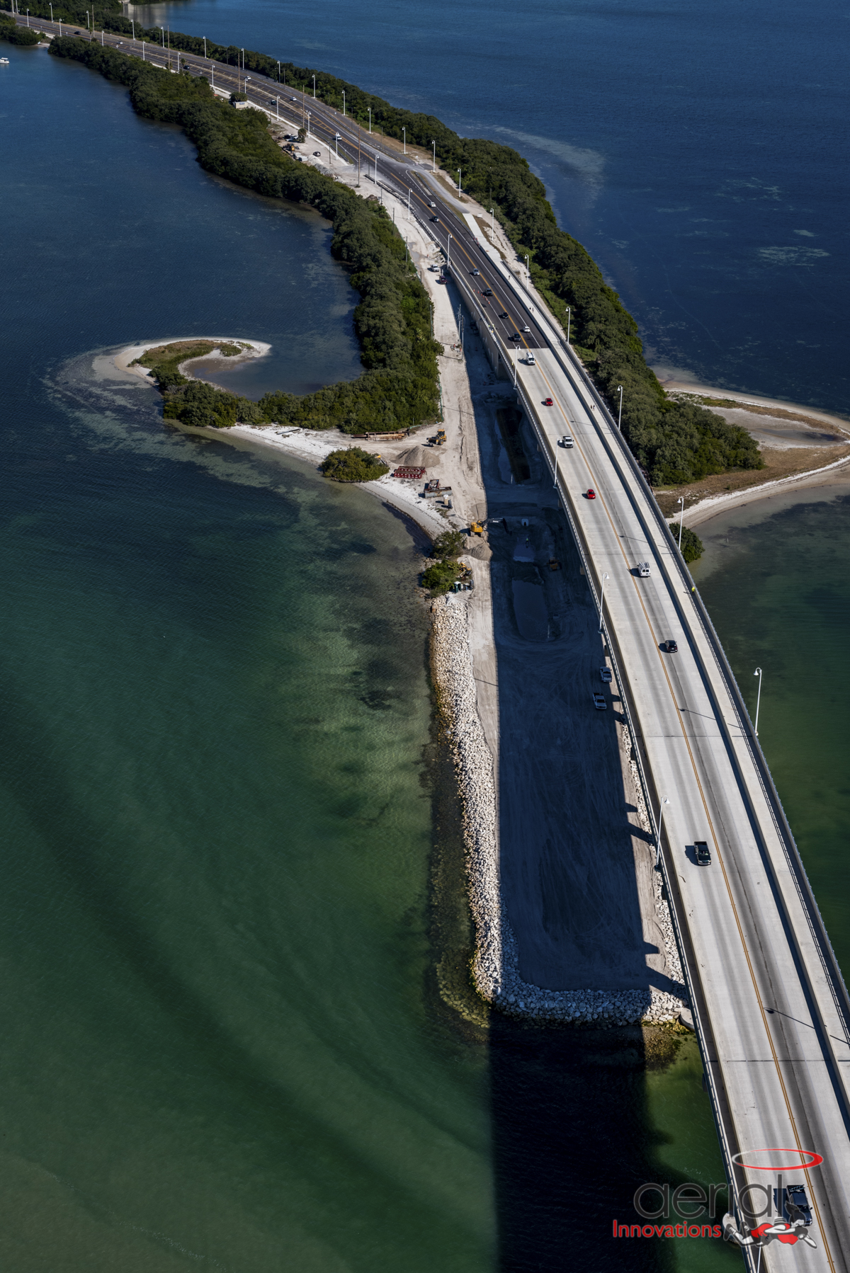 Aerial view of a bridge over blue water, connecting lush green land. Logo: Aerial Innovations