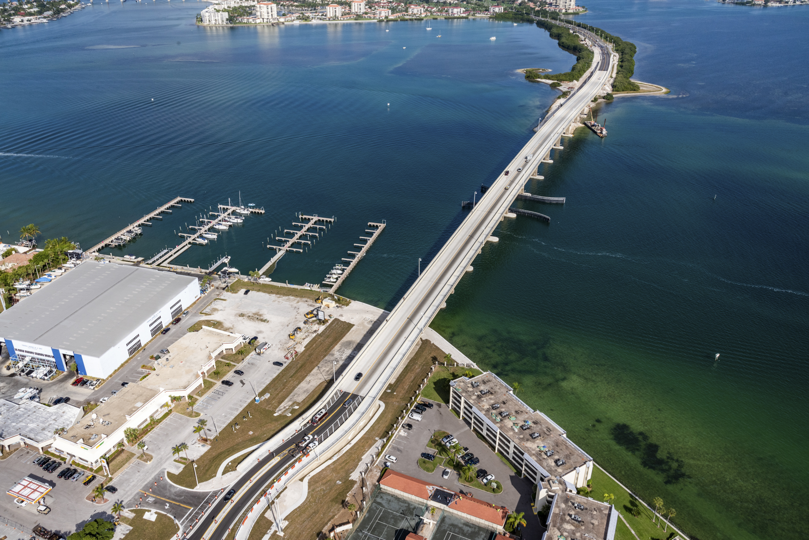 Aerial view of a long bridge spanning turquoise waters with docks, a marina, and nearby buildings