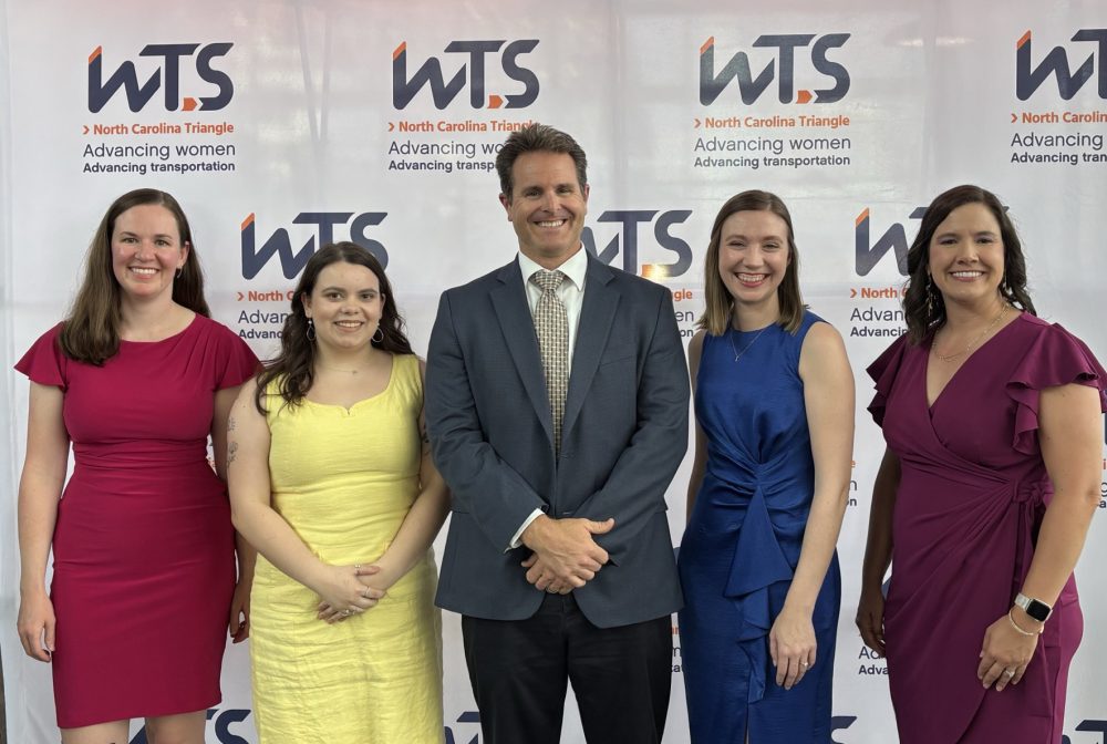 Five people smiling under neon "Raleigh" sign at WTS North Carolina Triangle event backdrop