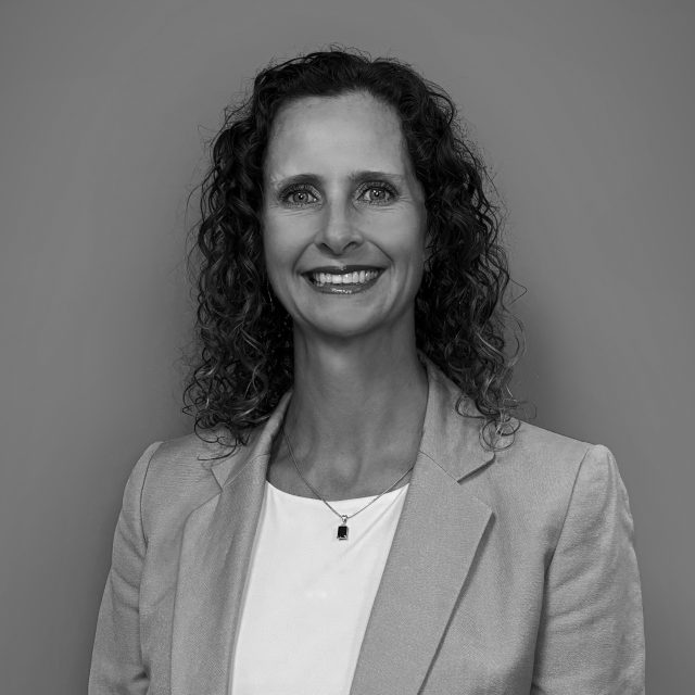 Erin, smiling woman in a blazer, against gray background