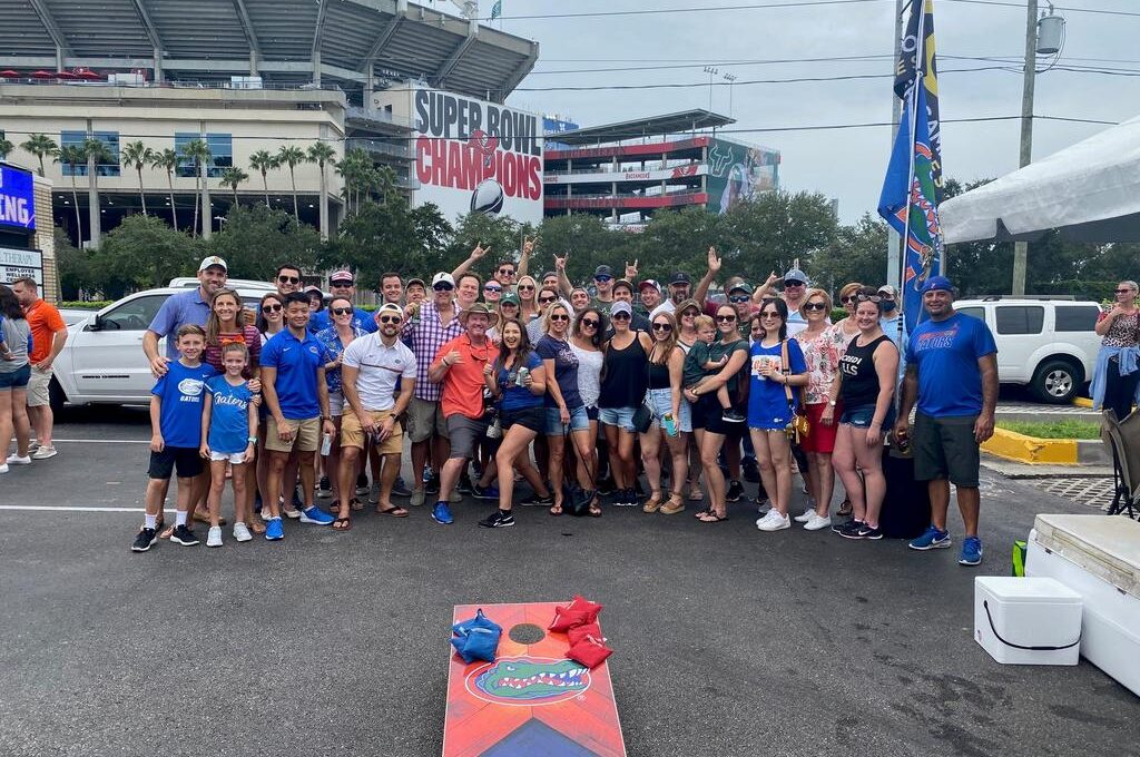 Large group of people tailgating outside a stadium with "Super Bowl Champions" banner, wearing Florida Gators attire
