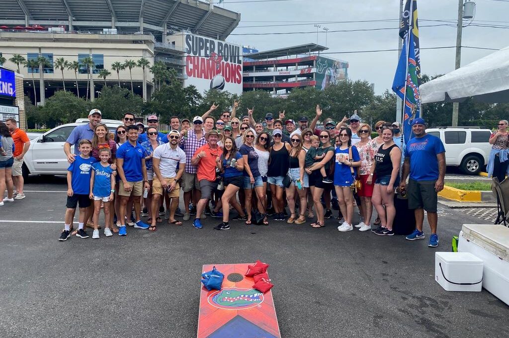 Large group of people tailgating outside a stadium with "Super Bowl Champions" banner, wearing Florida Gators attire